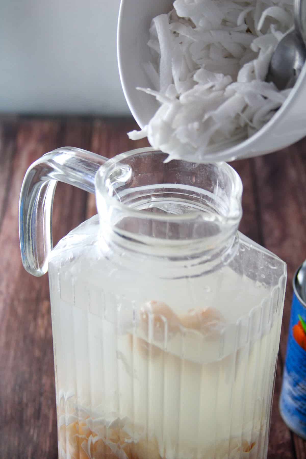 adding shredded buko to pitcher of coconut juice