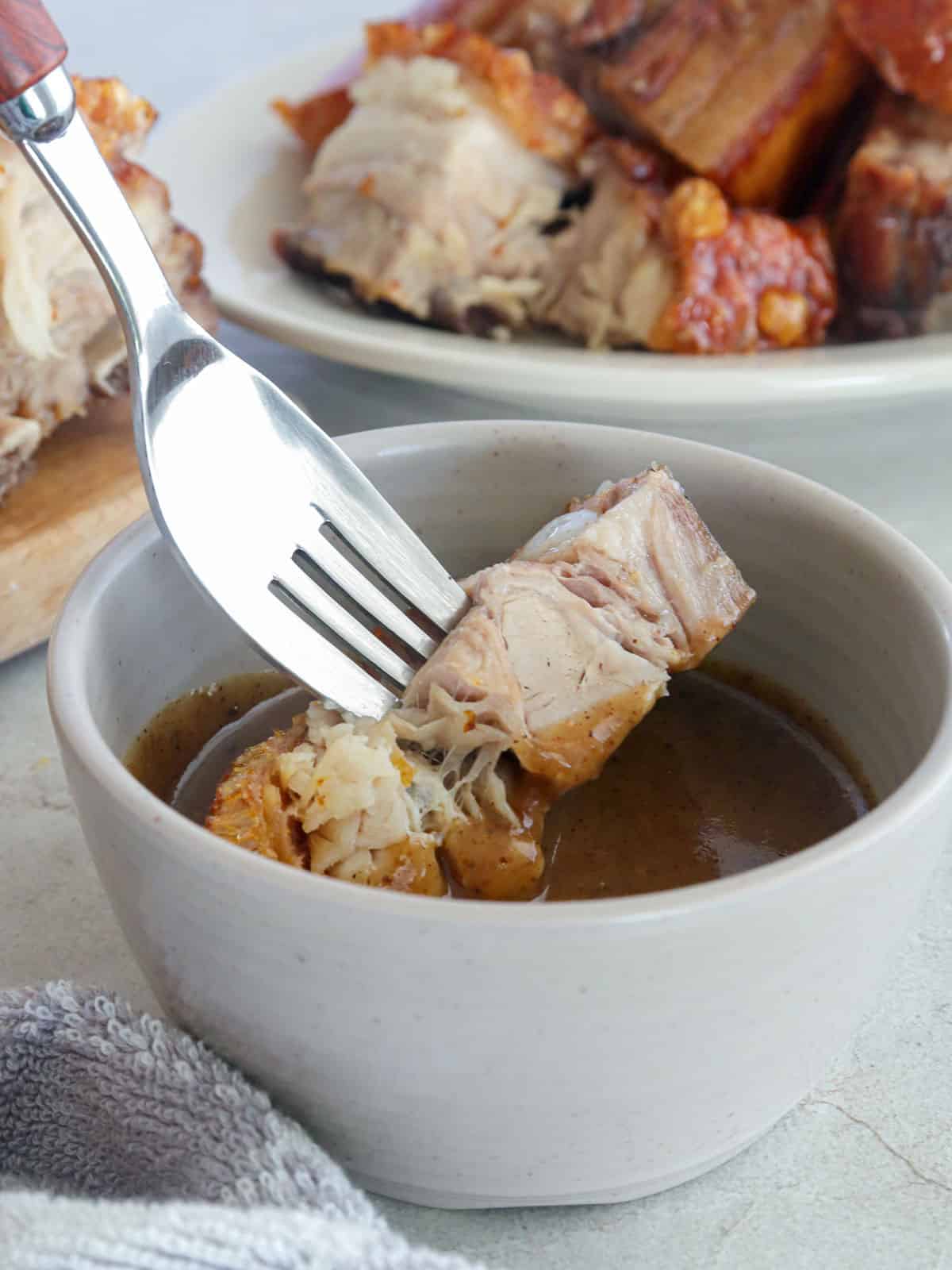 dipping chopped crispy pork belly in a white bowl of lechon sauce.