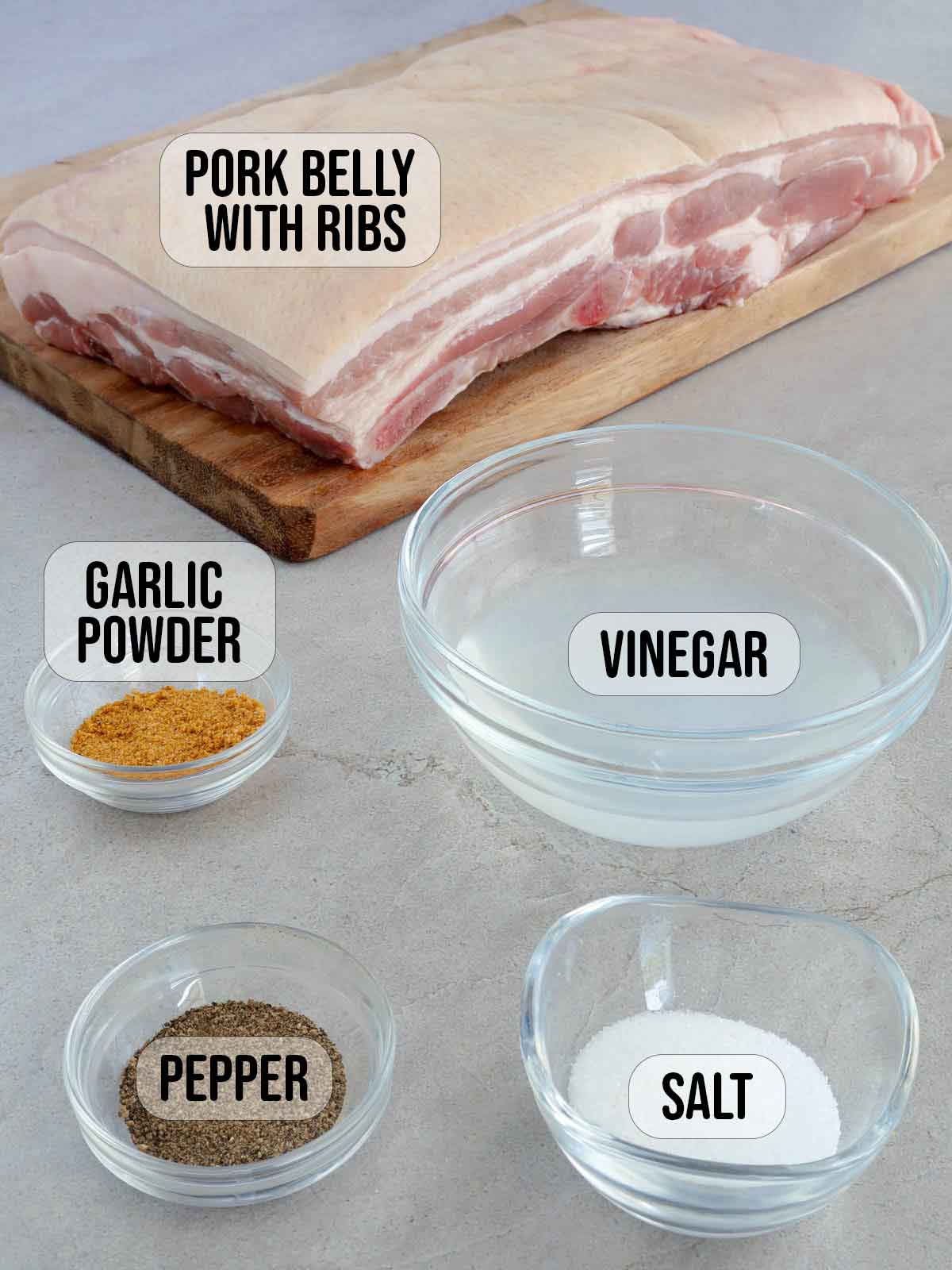 raw pork belly slab on a cutting board, garlic powder, salt, pepper, vinegar in bowsl.