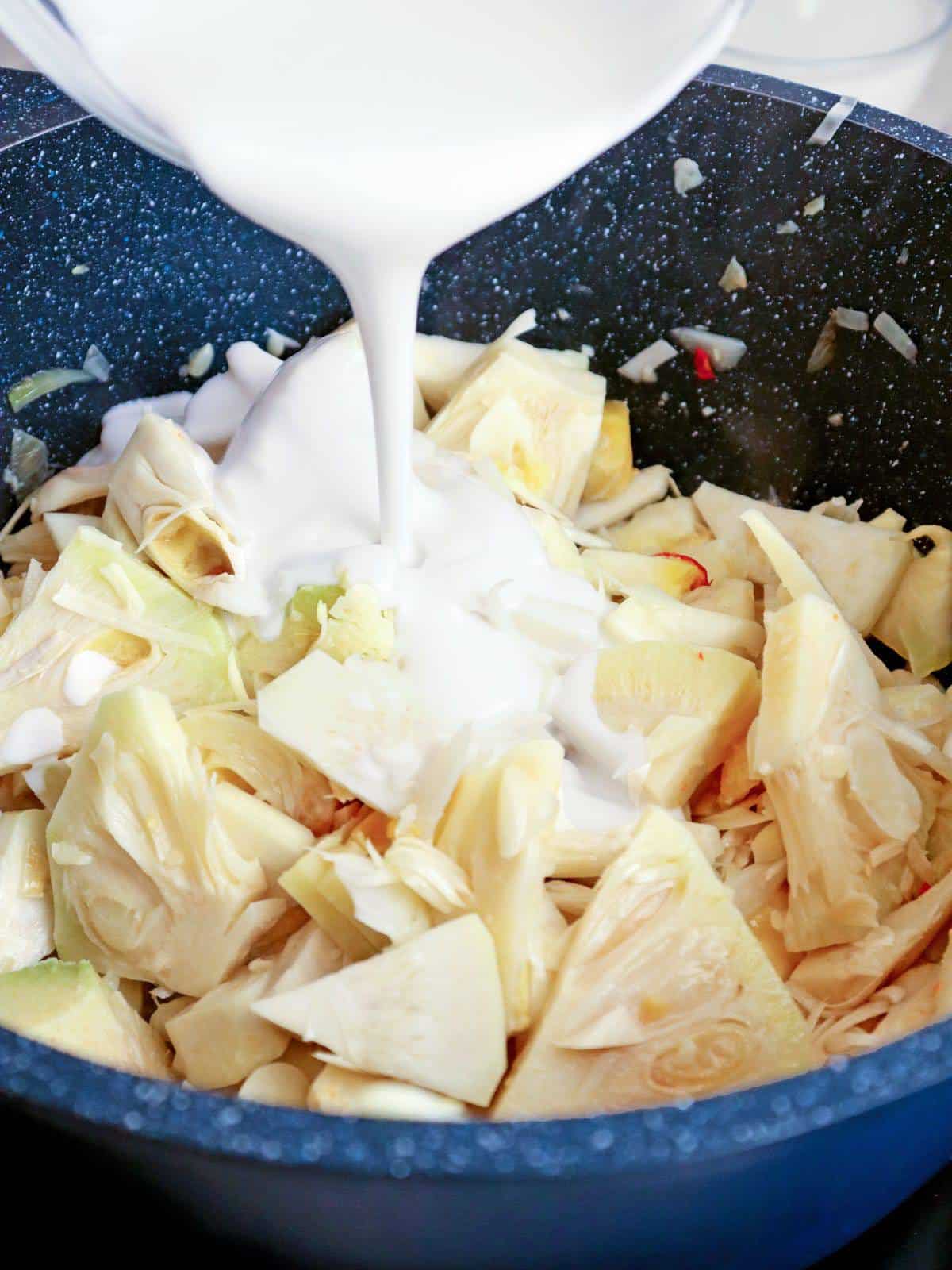 adding coconut milk to a pan of sliced jackfruit