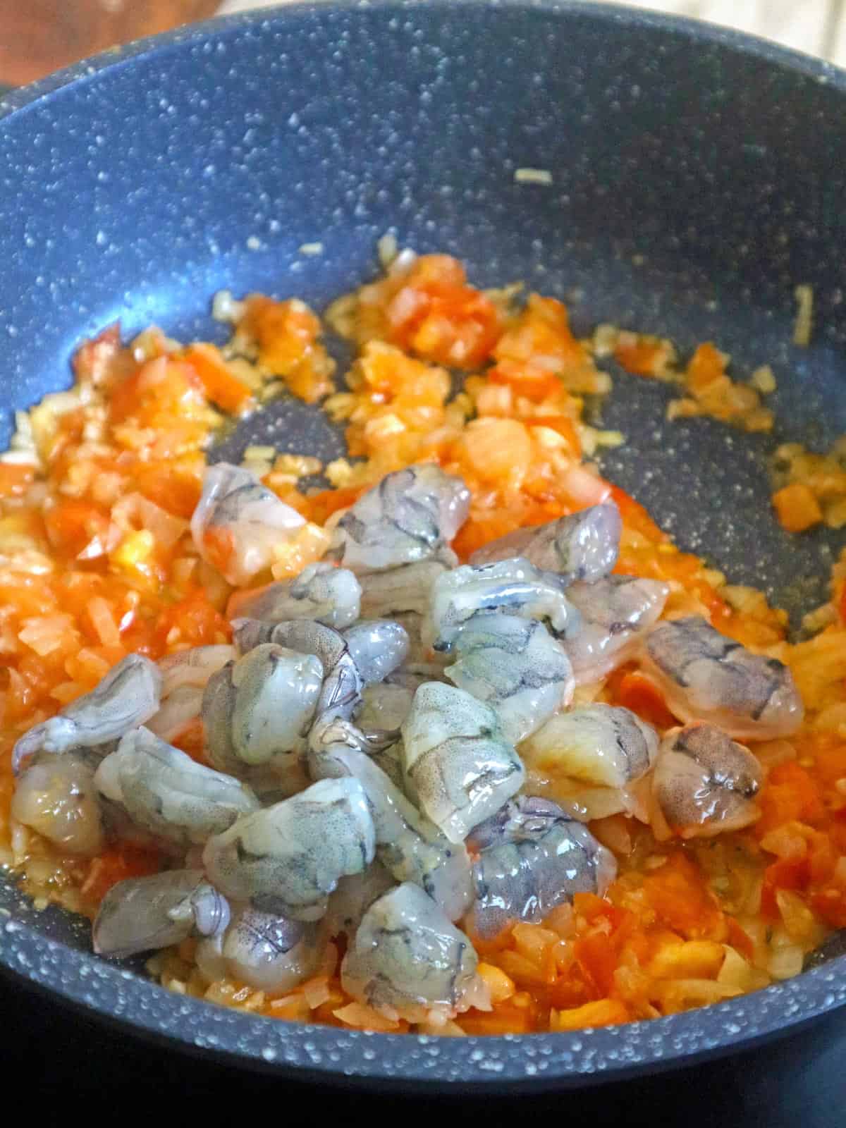 sauteing shrimp in onions, garlic, and tomatoes in a pan 