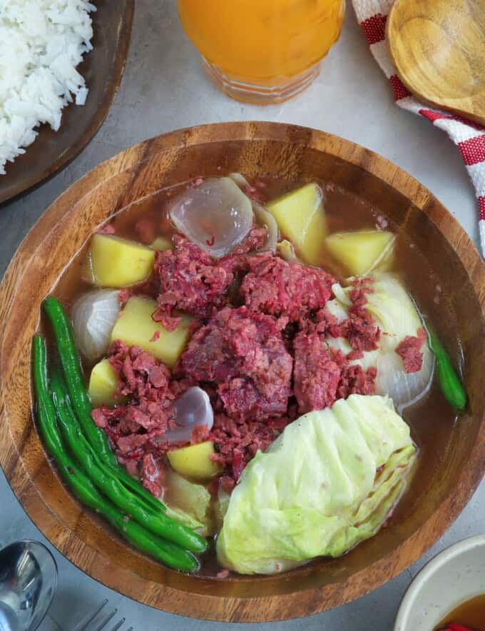 corned beef nilaga in a wooden bowl with a plate of rice on the side