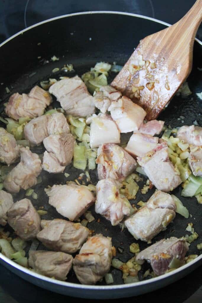 browning cubes of pork belly with onions and garlic in a pan