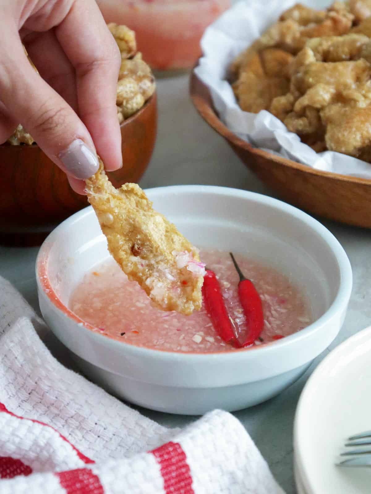 dipping tsitsarong manok in a bowl of spicy vinegar