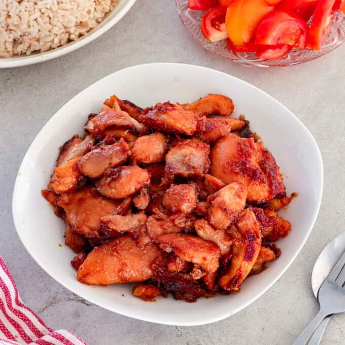 Chicken Tocino in a white serving bowl with garlic fried rice and sliced tomatoes in the background.