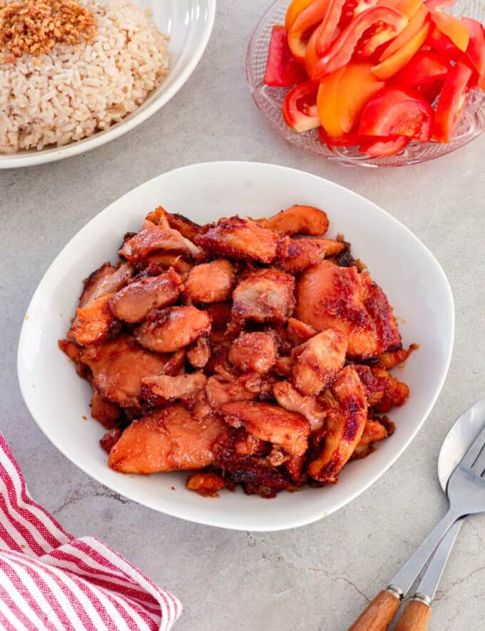 Chicken Tocino in a white serving bowl with garlic fried rice and sliced tomatoes in the background.
