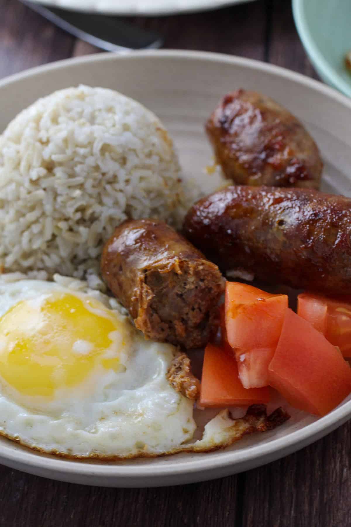 fried rice, fried egg, sliced tomatoes, and longganisa on a plate.