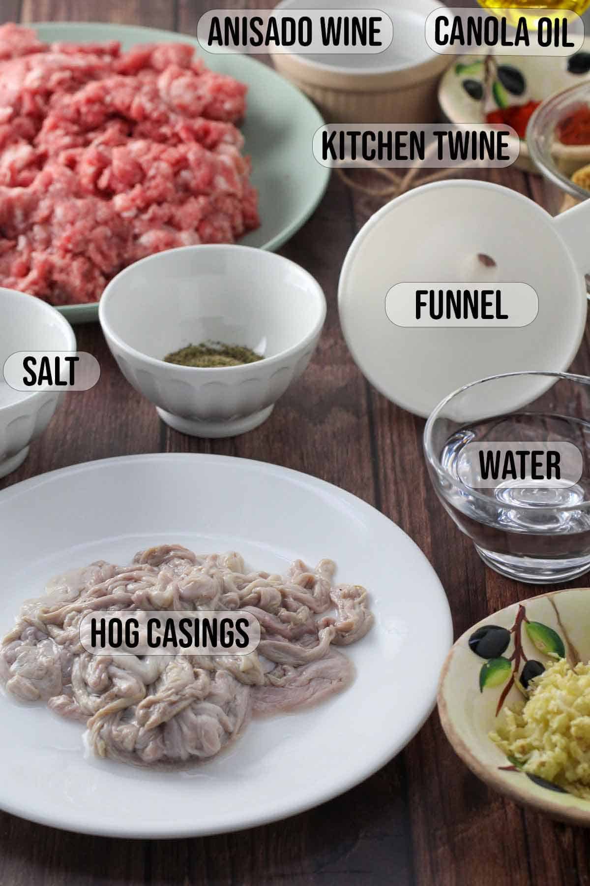 hog casings, ground pokr, funnel, salt, anisado wine, garlic, water, canola oil in bowls.