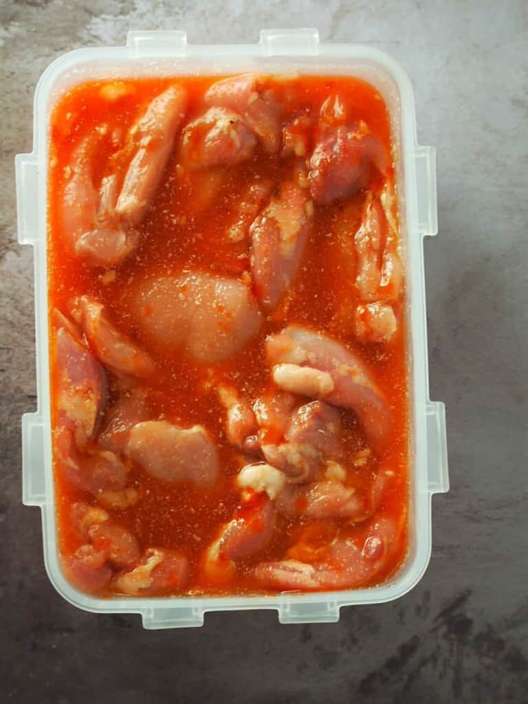 boneless chicken thigh meat marinating in a plastic container to make tocino