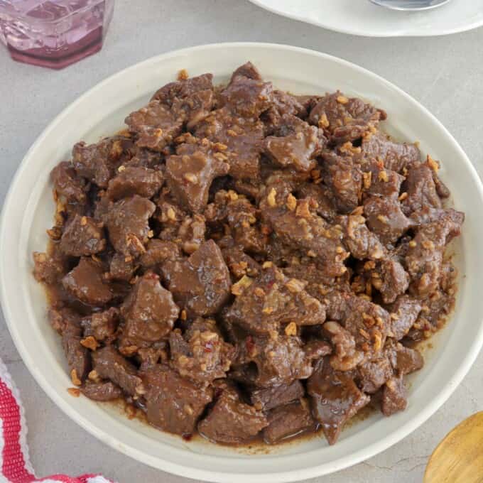 Beef Salpicao on a serving plate with steamed rice and glass of water in the background.