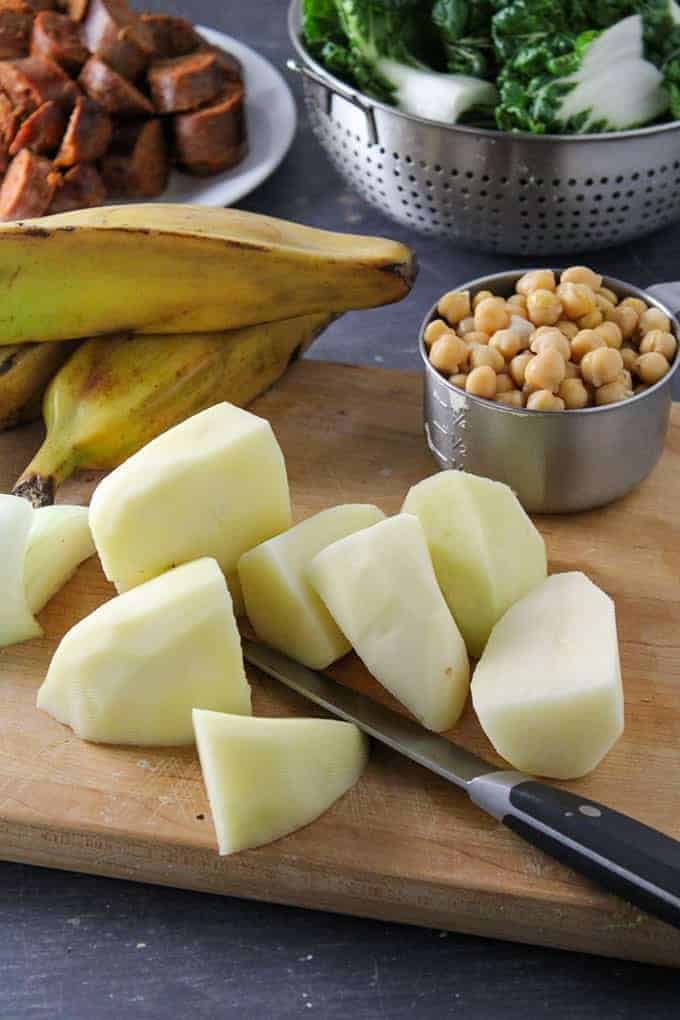 peeled and quartered potatoes, saba bananas, garbanzo beans on a wooden cutting board