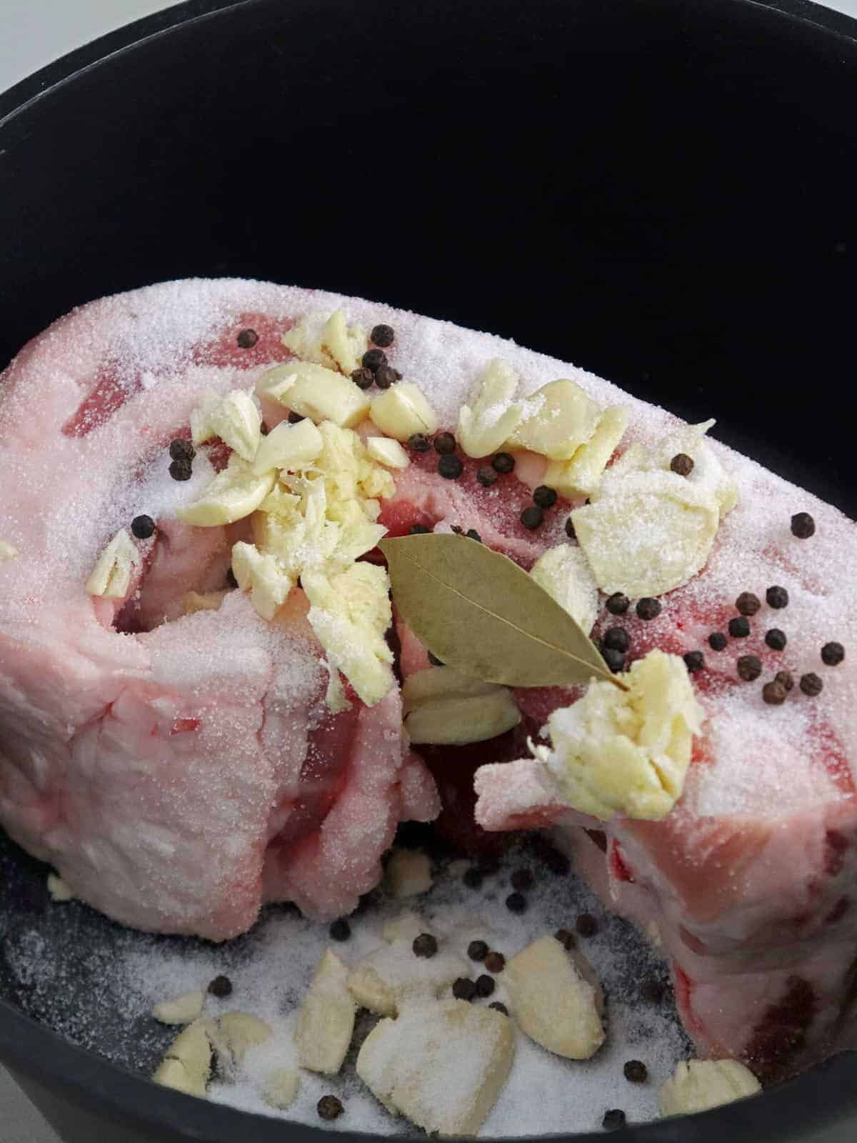 raw pork belly slab with crushed onions, bay leaves, peppercorns, and salt in a pot to boil