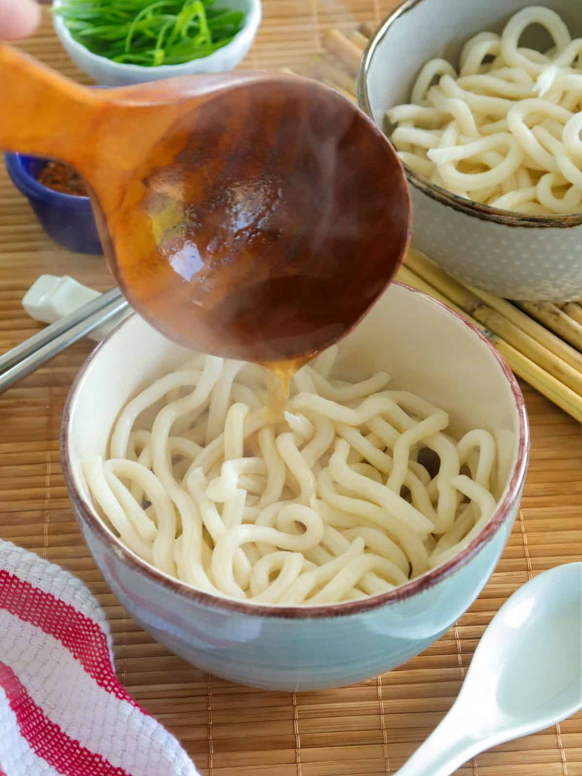 pouring noodle broth over udon noodles in a bowl