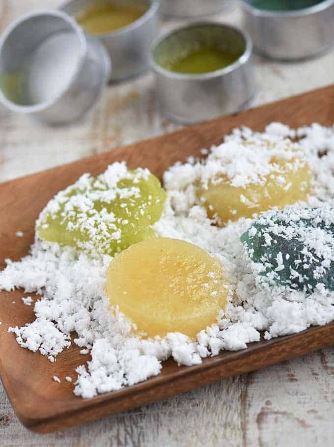 coating steamed pitsi-pitsi in grated coconut on a wooden platter