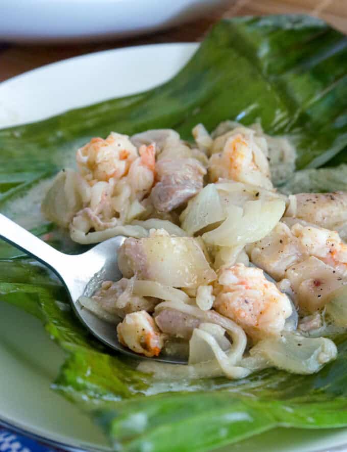 eating pinais na hipon with a spoon on a banana leaf-lined white plate.