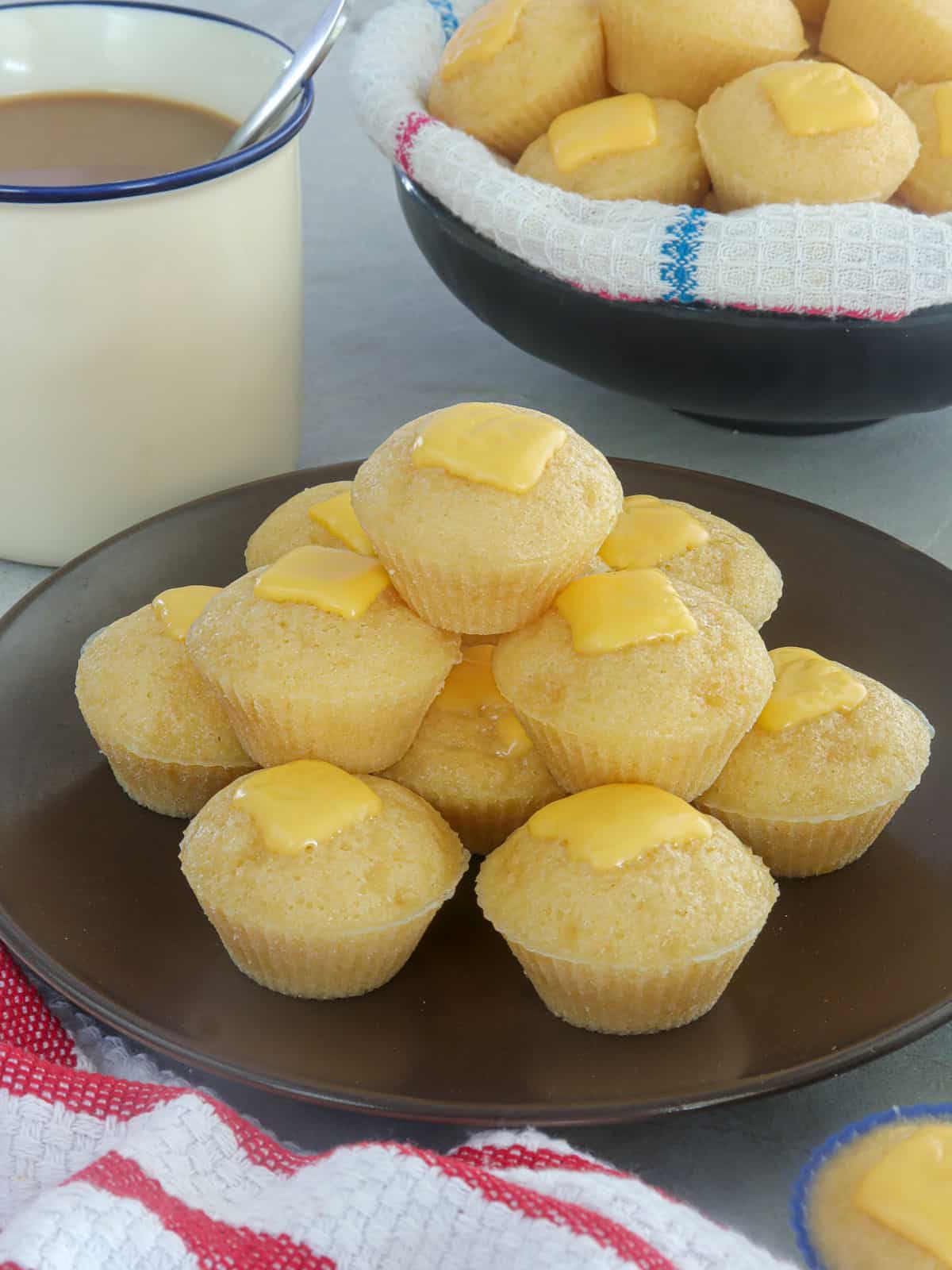 Cheese Puto on a brown serving plate with cup of coffee in the background.