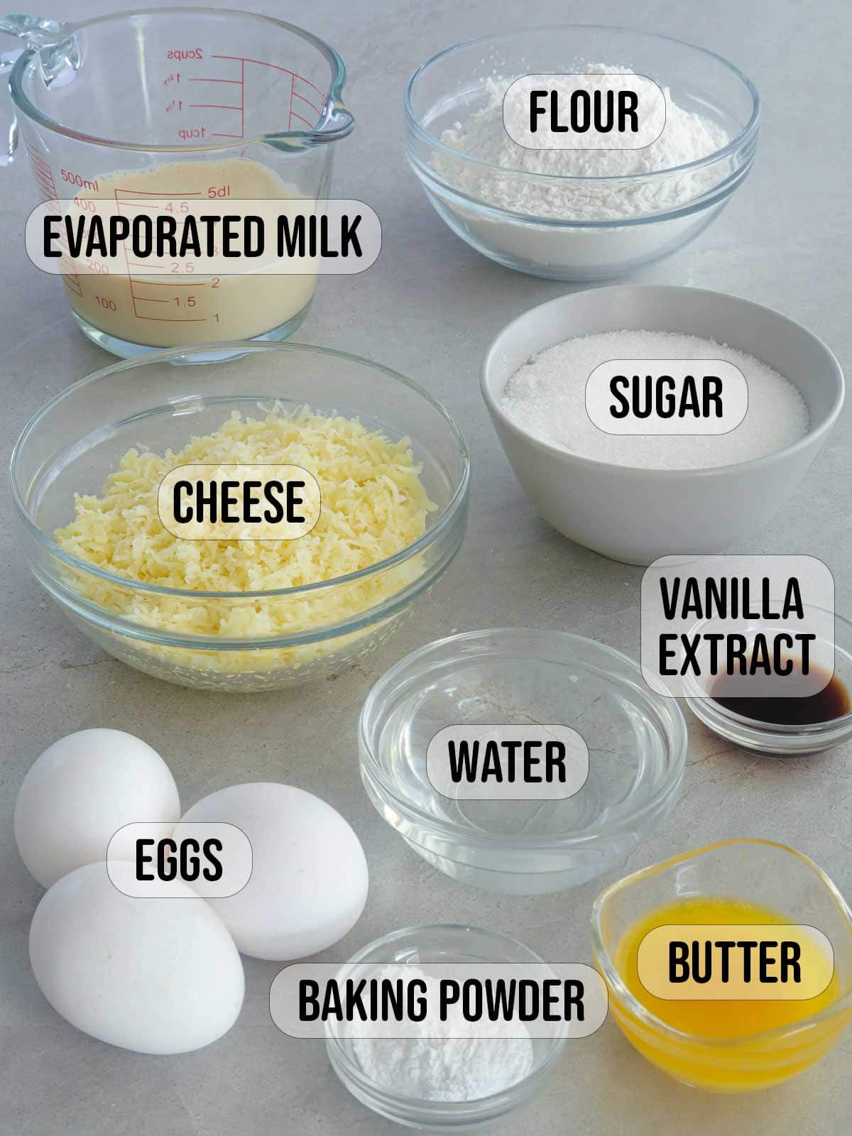 evaporated milk, flour, baking powder, eggs, butter, water, sugar, flour, vanilla extract, shredded cheese in bowls.