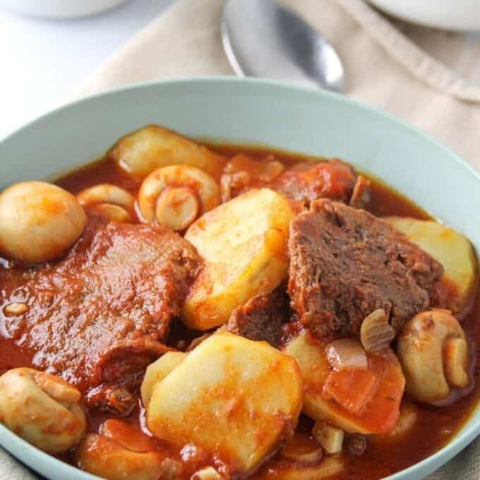 ox tongue stew with mushrooms and potatoes in a blue serving bowl