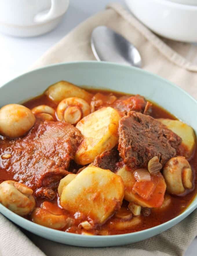 ox tongue stew with mushrooms and potatoes in a blue serving bowl