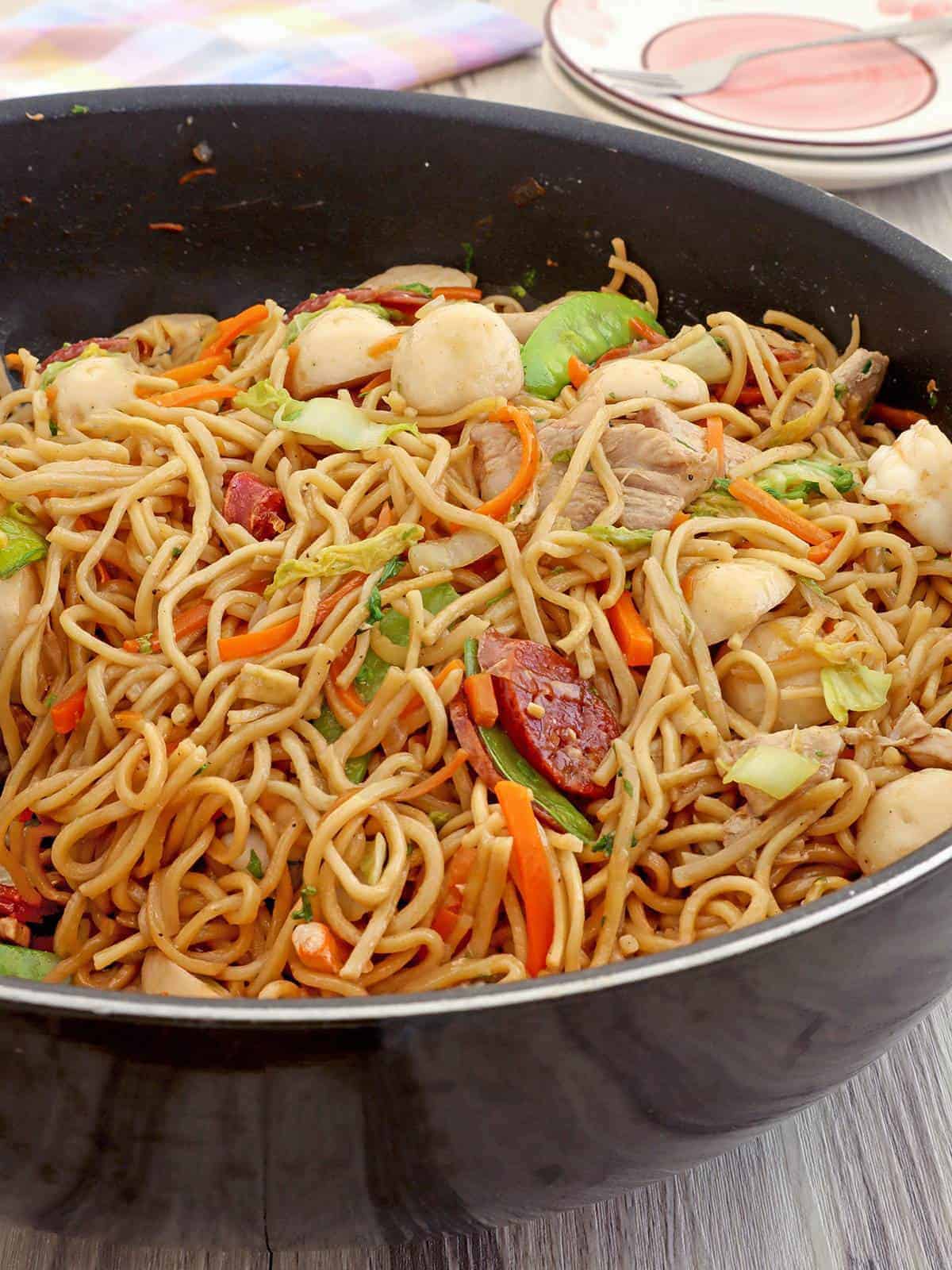 Pancit canton Guisado with fish balls, sausage, snow peas, carrots, cabbage n a wok