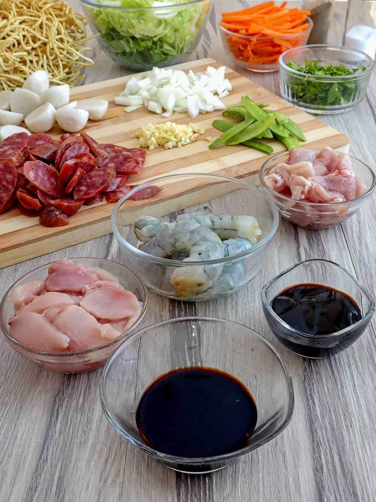 peeled shrimp, sliced sausage, sliced carrots, cut chicken, chopped onions, minced garlic, pancit canton, chicken broth in bowls