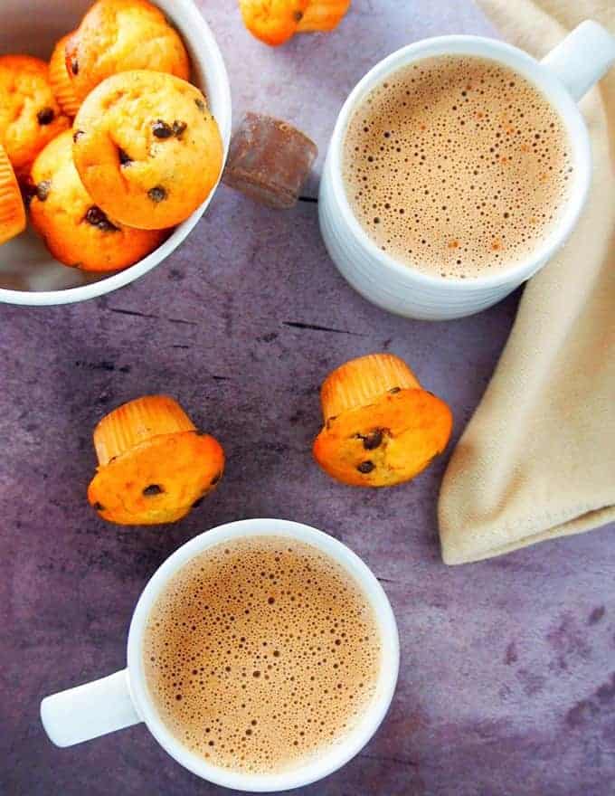 top view of Filipino hot chocolate in white cups with a bowl of fruit muffins on the side