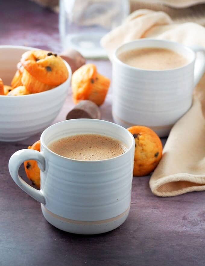 Tsokolate in white cups with a bowl of muffins on the side