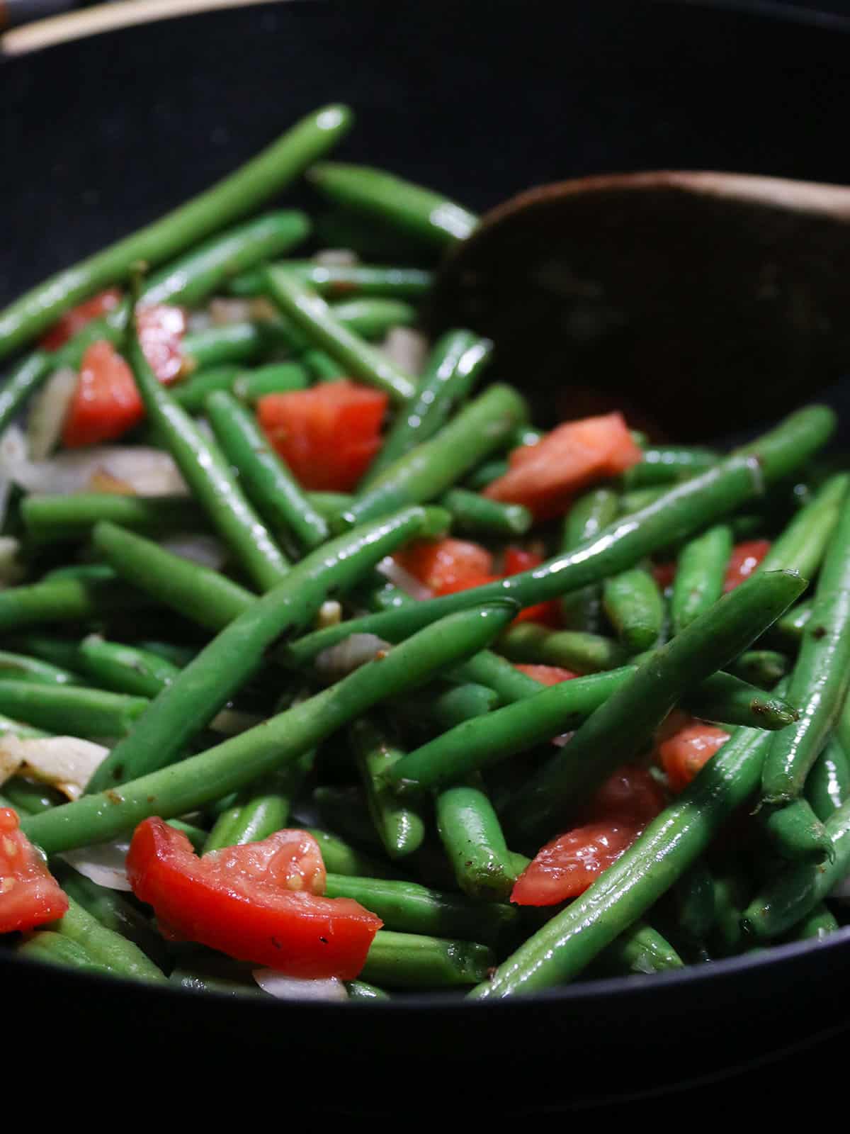 sauteing green beans with tomatoes in a wok