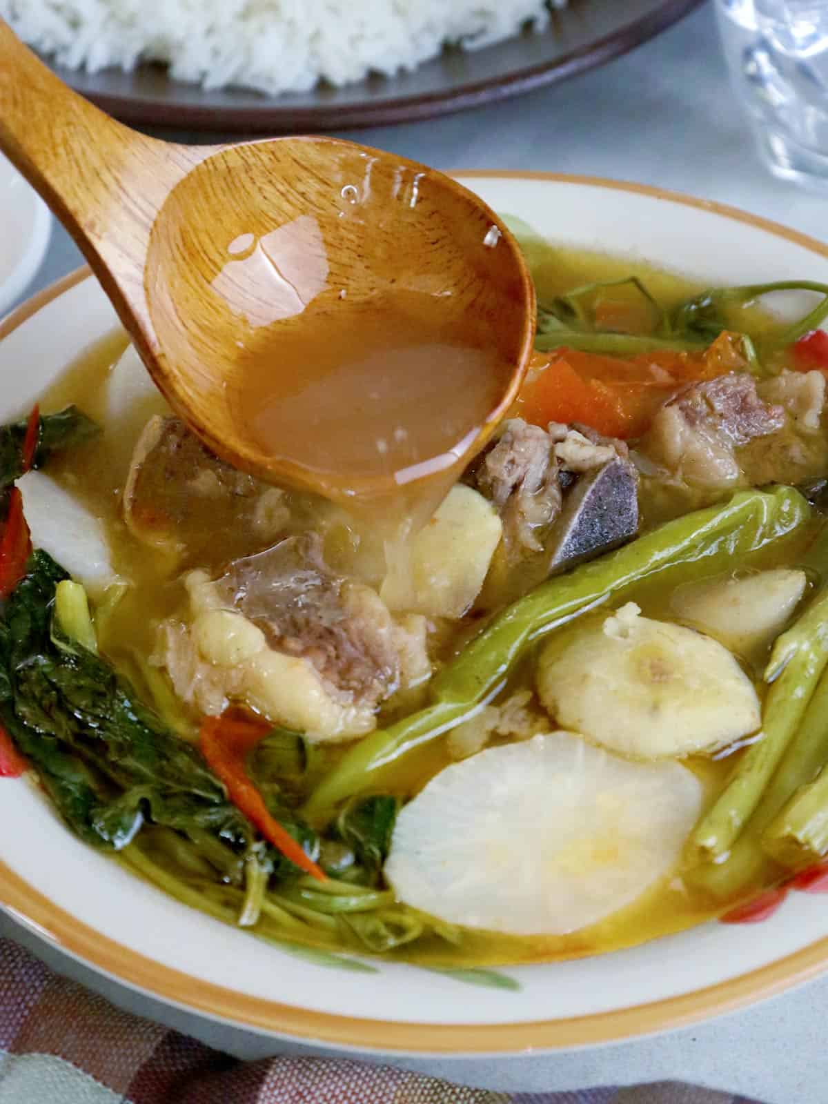 pouring broth in a bowl of beef sinigang with a wooden spoon.