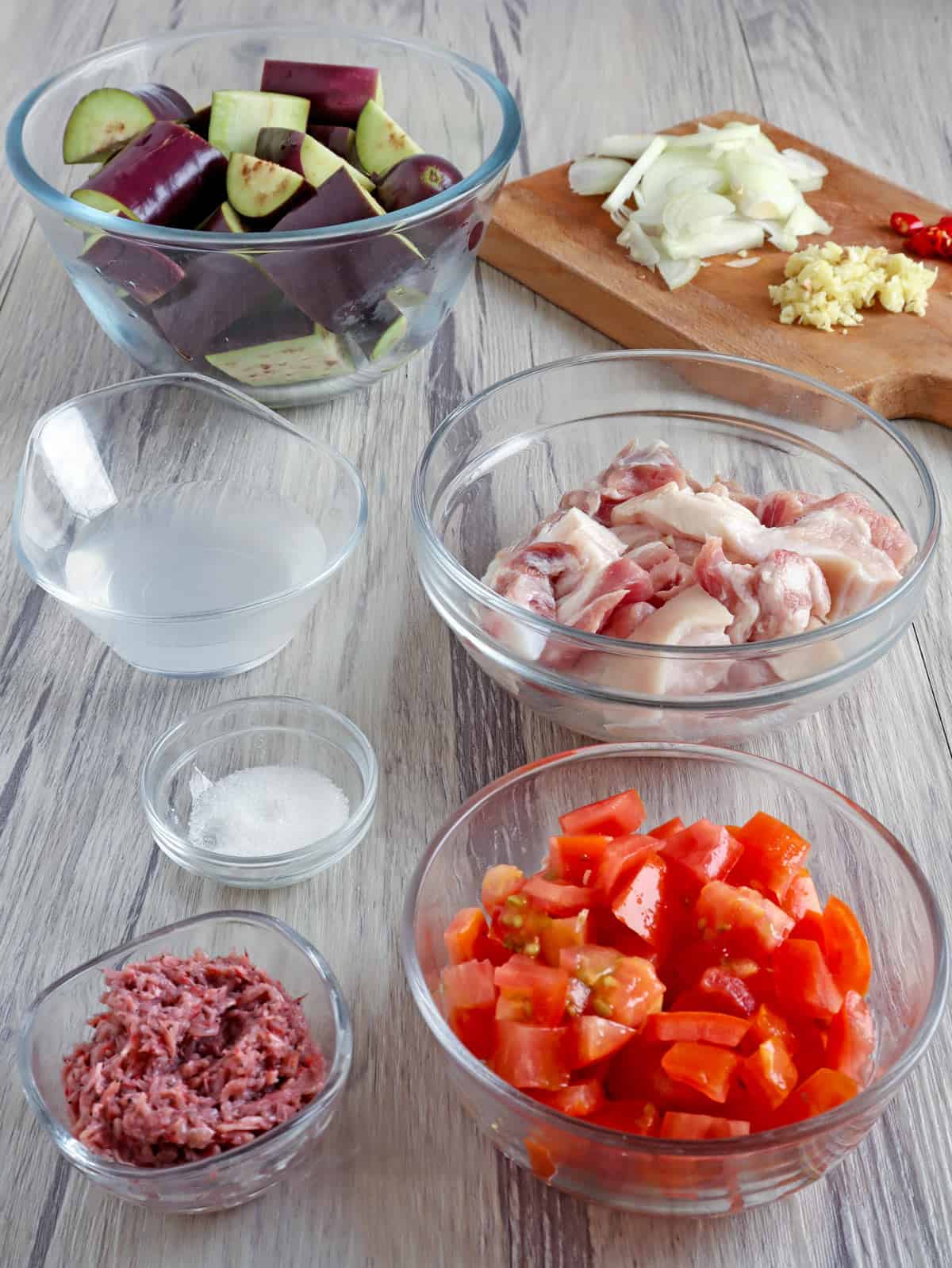 eggplant, chopped onions, tomatoes, garlic, vinegar, salt, shrimp paste in clear bowls