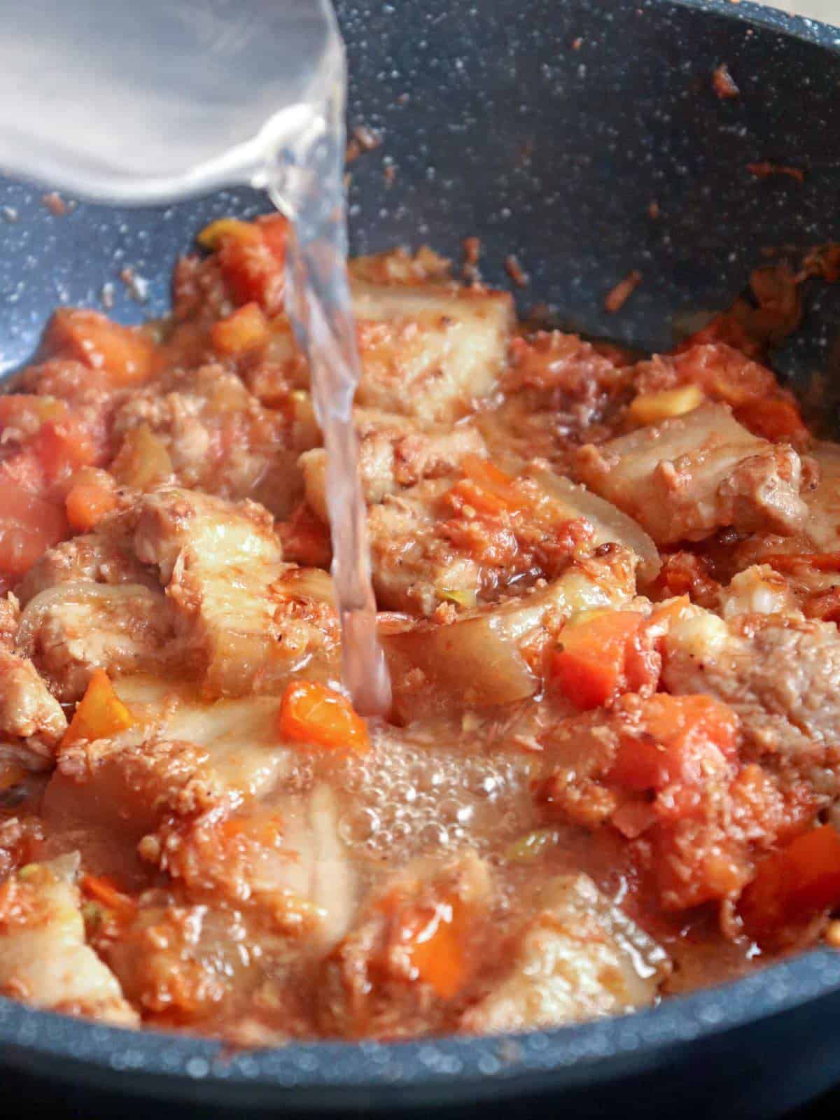 adding water to sauteed pork belly in a pan