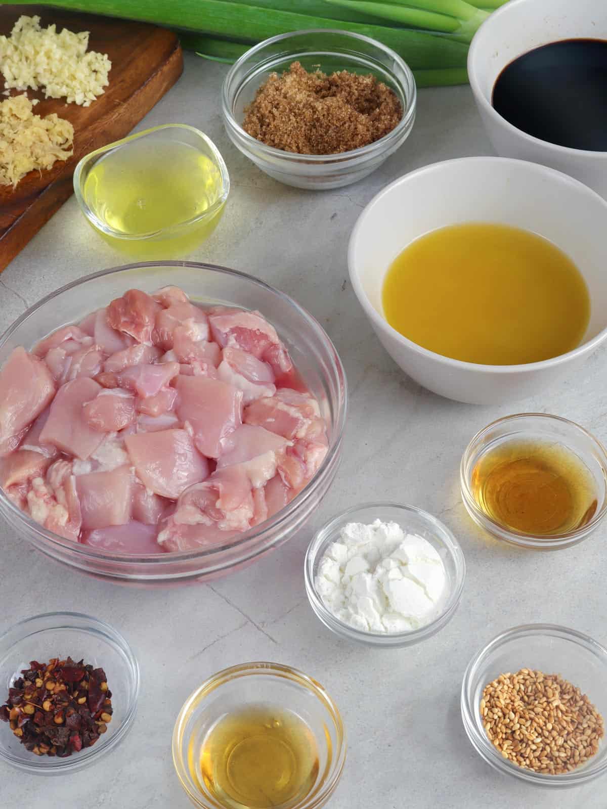 cubed chicken thighs, calamansi juice, soy sauce, red chili flakes, brown sugar, Chinese cooking wine, garlic, ginger, cornstarch, oil, sesame seeds, green onions in bowls