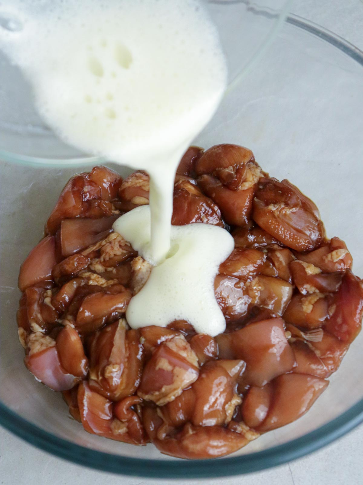 pouring batter in a bowl of marinated chicken cubes