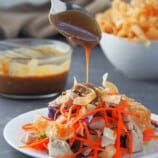 pouring peanut dressing on a plate of salad