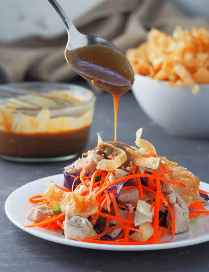 pouring peanut dressing on a plate of salad