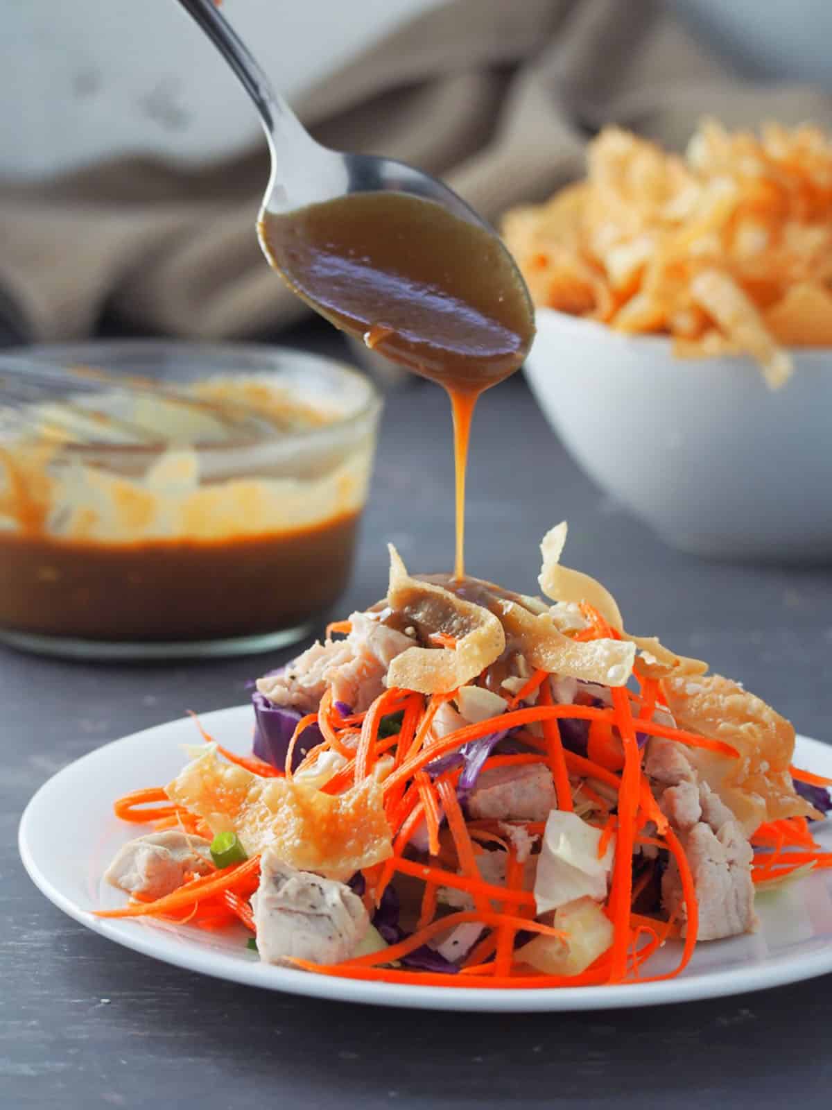 pouring peanut dressing on a plate of salad.