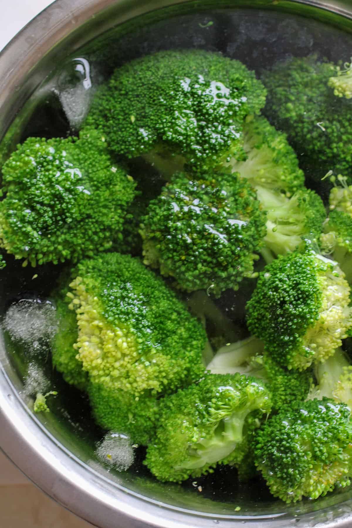 blanching broccoli florets in a bowl of iced water
