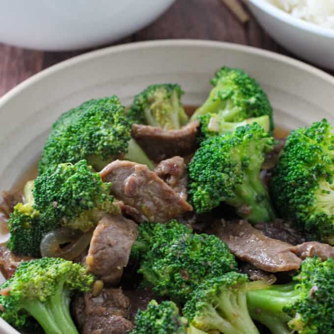 Beef Broccoli in a serving bowl with a plate of steamed rice on the side