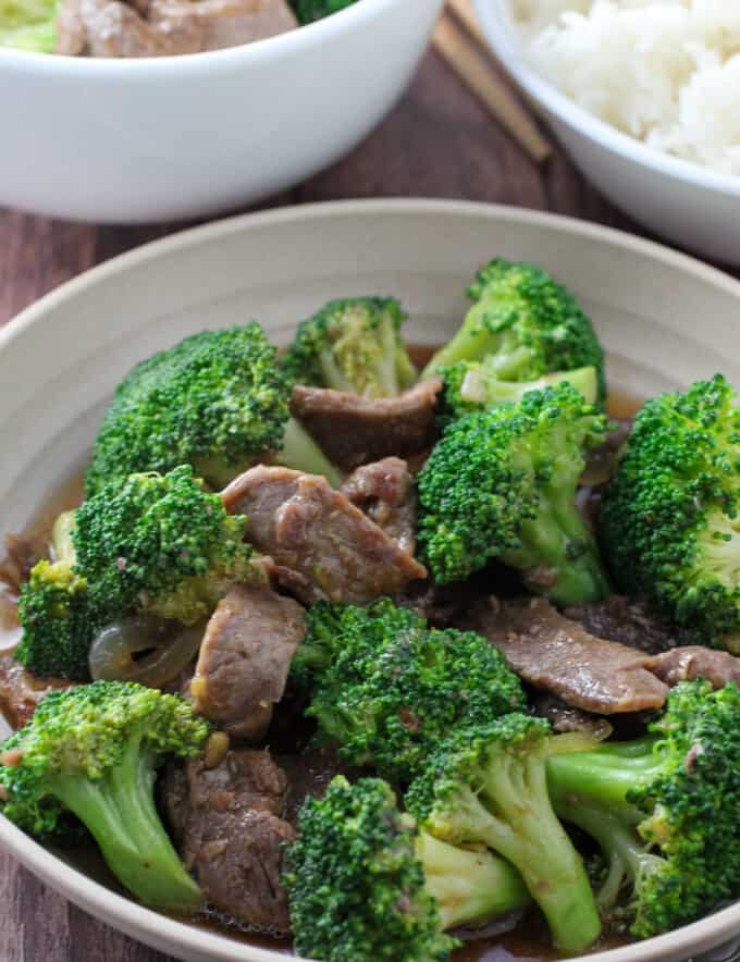 Beef Broccoli in a serving bowl with a plate of steamed rice on the side