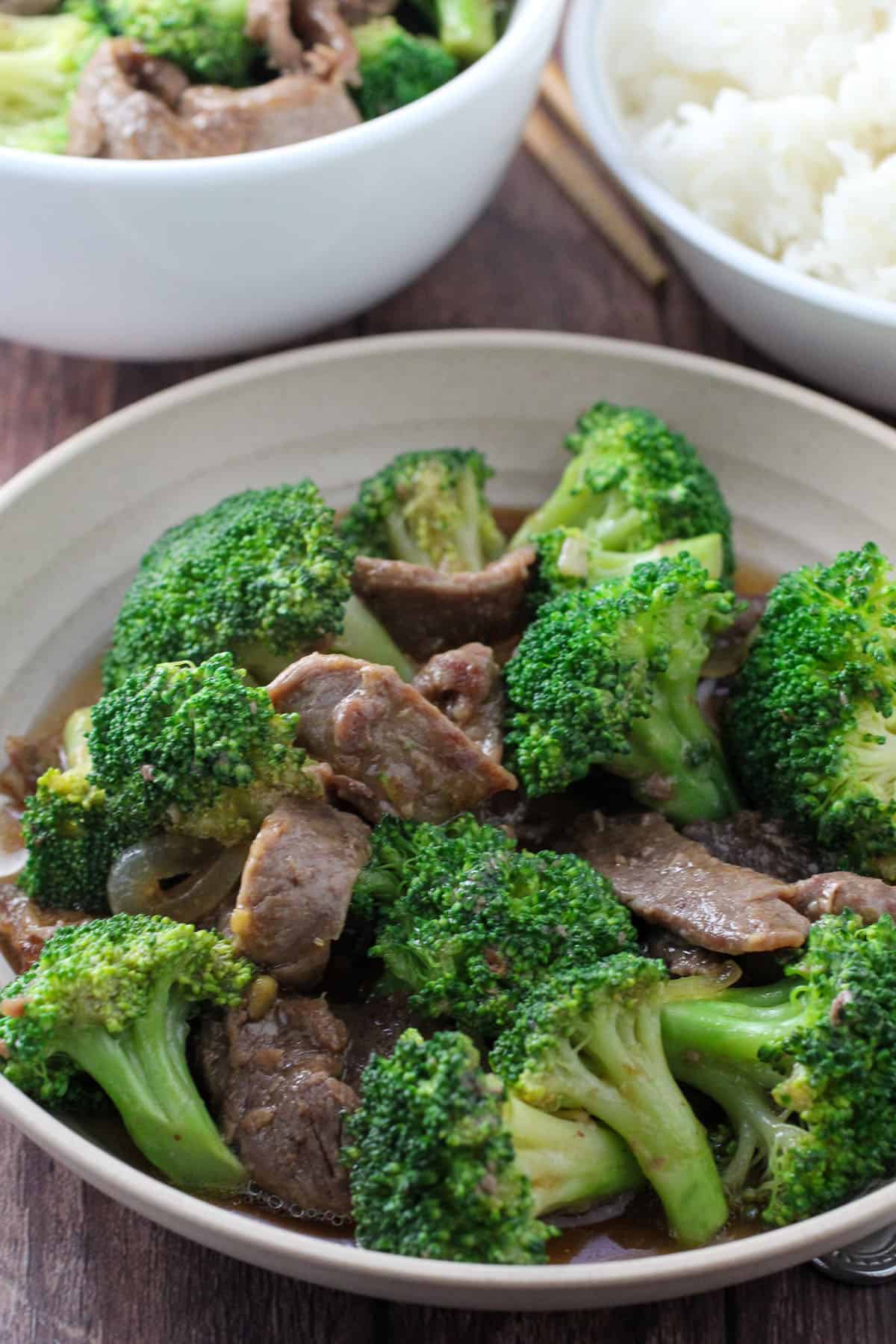 Beef Broccoli in a serving bowl with a plate of steamed rice on the side