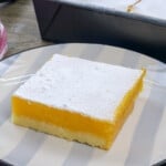 slice of calamansi bars on a serving plate with a baking pan of bars in the background.