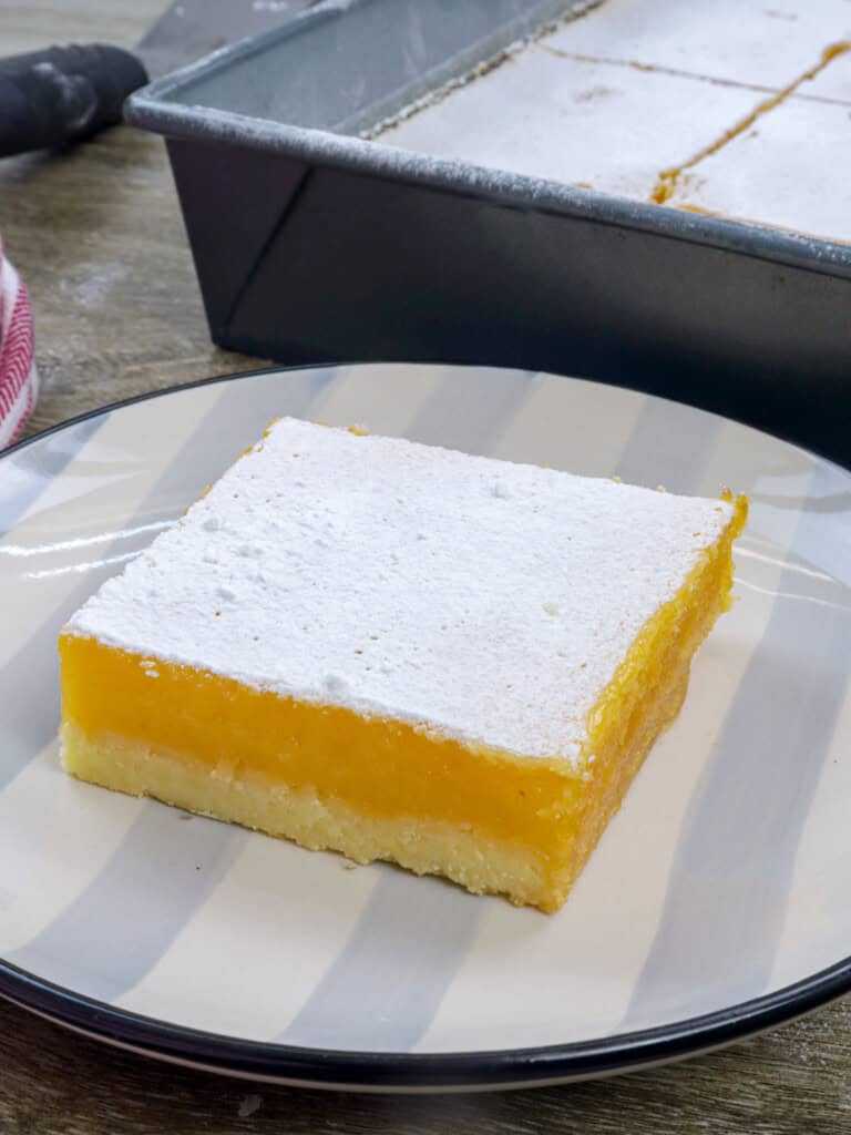 slice of calamansi bars on a serving plate with a baking pan of bars in the background.