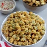 breaded fried okra in a white bowl with spicy vinegar dipping sauce on the side