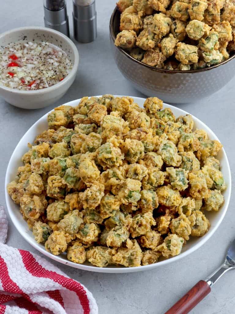 breaded fried okra in a white bowl with spicy vinegar dipping sauce on the side