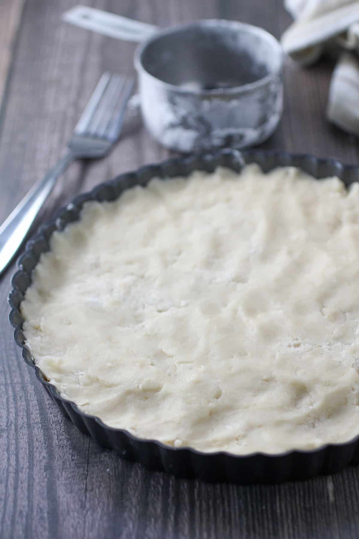 shortbread dough in a round pan with measuring cup and fork in the background.