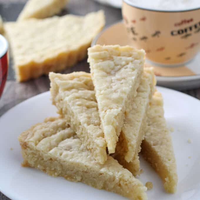 shortbread cookie wedges on a white plate with cup of coffee in the background.