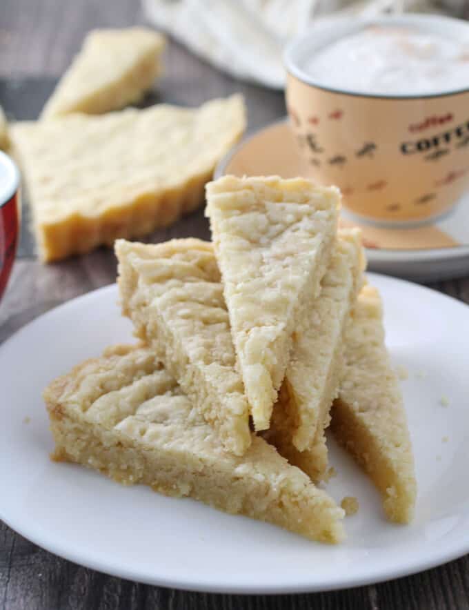 shortbread cookie wedges on a white plate with cup of coffee in the background.