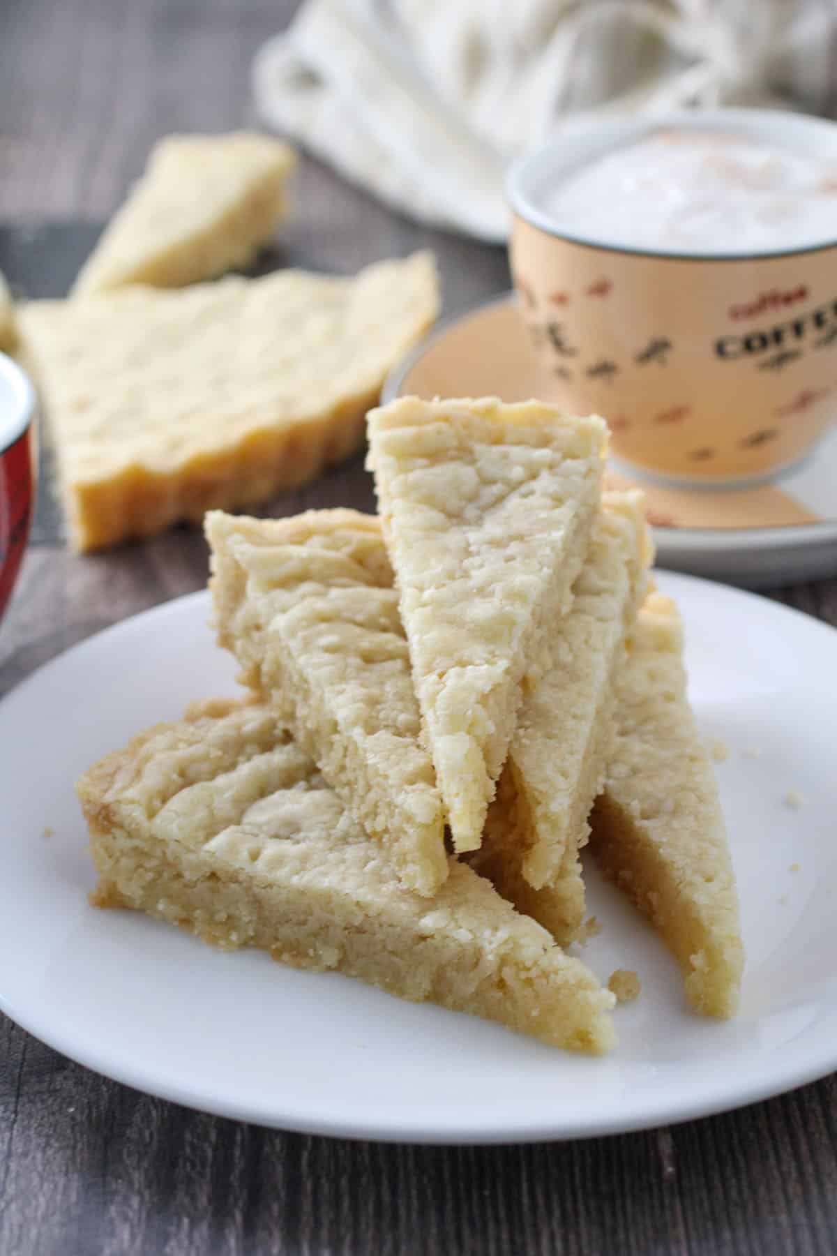 shortbread cookie wedges on a white plate with cup of coffee in the background.