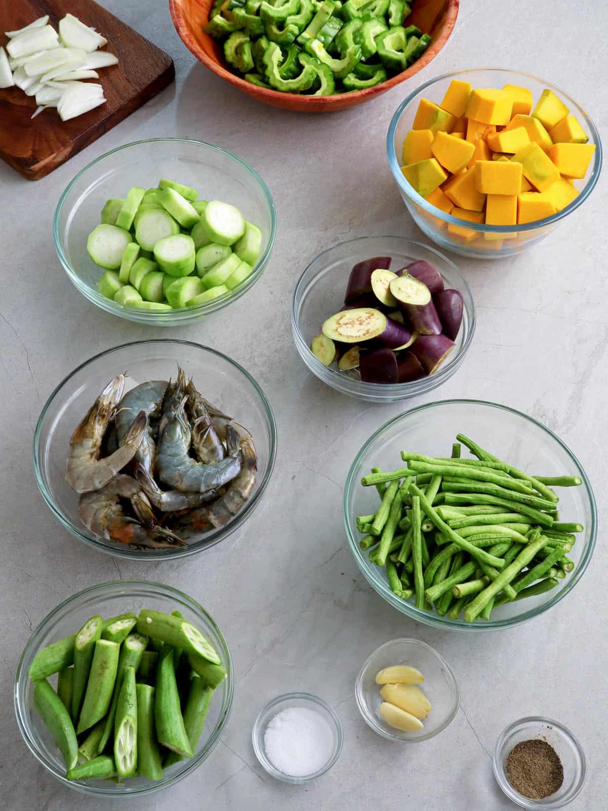 eggplant, calabasa, shrimp, sitaw, okra, patola, ampalaya, onion, garlic, and salt in bowls