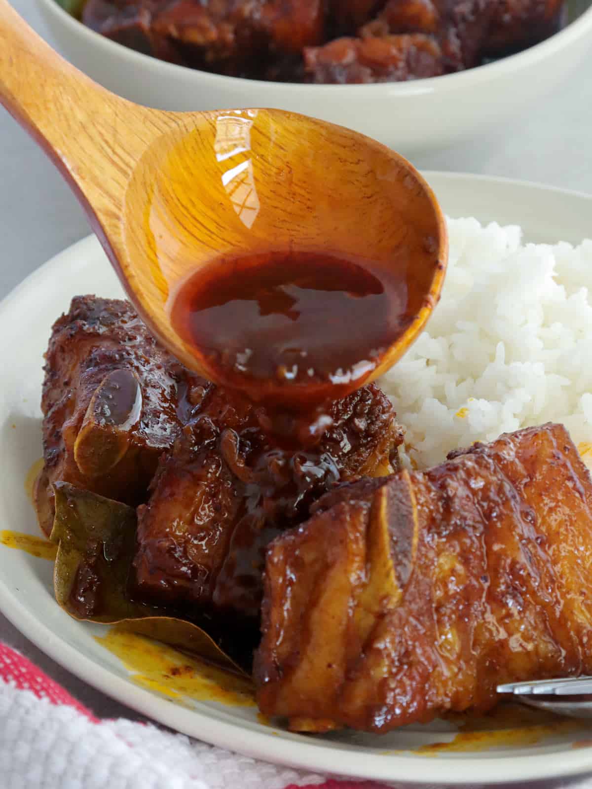 pouring sauce over adobong pula with steamed rice on a white plate